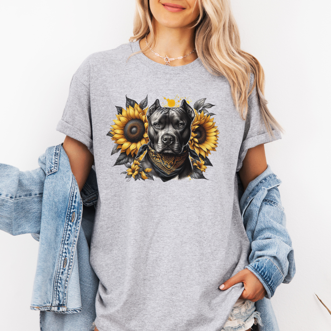 A woman wearing a grey graphic t-shirt with a printed design of a dark coloured pitbull dog wearing a black and gold bandana, surrounded by yellow sunflowers. Grab your tee from Coffee and Moo NZ.