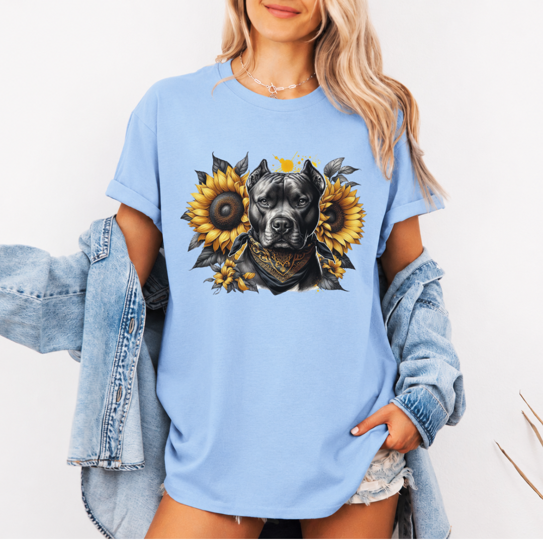 A woman wearing a baby blue graphic t-shirt with a printed design of a dark coloured pitbull dog wearing a black and gold bandana, surrounded by yellow sunflowers. Grab your tee from Coffee and Moo NZ.