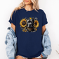A woman wearing a navy graphic t-shirt with a printed design of a dark coloured pitbull dog wearing a black and gold bandana, surrounded by yellow sunflowers. Grab your tee from Coffee and Moo NZ.