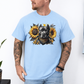 A man wearing a light blue short-sleeve graphic t-shirt featuring a detailed print of a pitbull dog wearing a bandana and surrounded by yellow sunflowers. The man has tattoos on both arms and is wearing light blue jeans, standing against a white wall. Grab your tee from coffee and moo NZ.