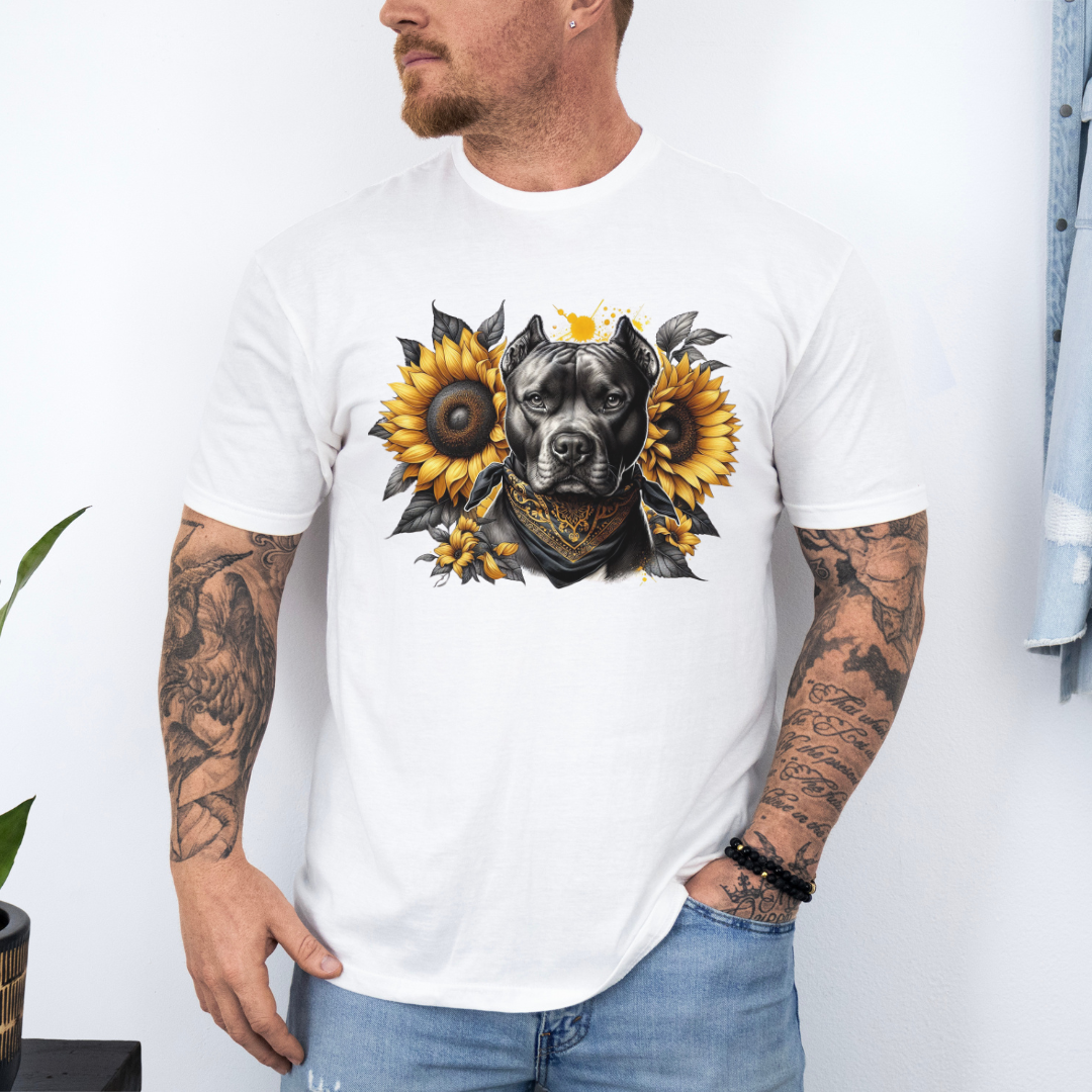 A man wearing a white short-sleeve graphic t-shirt featuring a detailed print of a pitbull dog wearing a bandana and surrounded by yellow sunflowers. The man has tattoos on both arms and is wearing light blue jeans, standing against a white wall. Grab your tee from coffee and moo NZ.