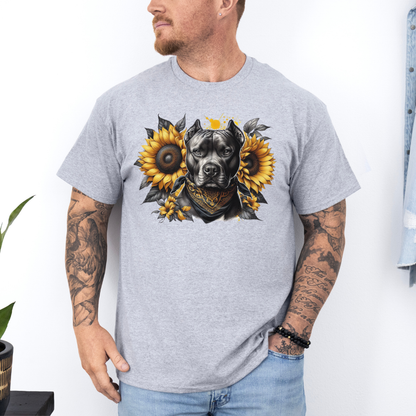 A man wearing a grey short-sleeve graphic t-shirt featuring a detailed print of a pitbull dog wearing a bandana and surrounded by yellow sunflowers. The man has tattoos on both arms and is wearing light blue jeans, standing against a white wall. Grab your tee from coffee and moo NZ.