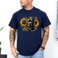 A man wearing a navy short-sleeve graphic t-shirt featuring a detailed print of a pitbull dog wearing a bandana and surrounded by yellow sunflowers. The man has tattoos on both arms and is wearing light blue jeans, standing against a white wall. Grab your tee from coffee and moo NZ.