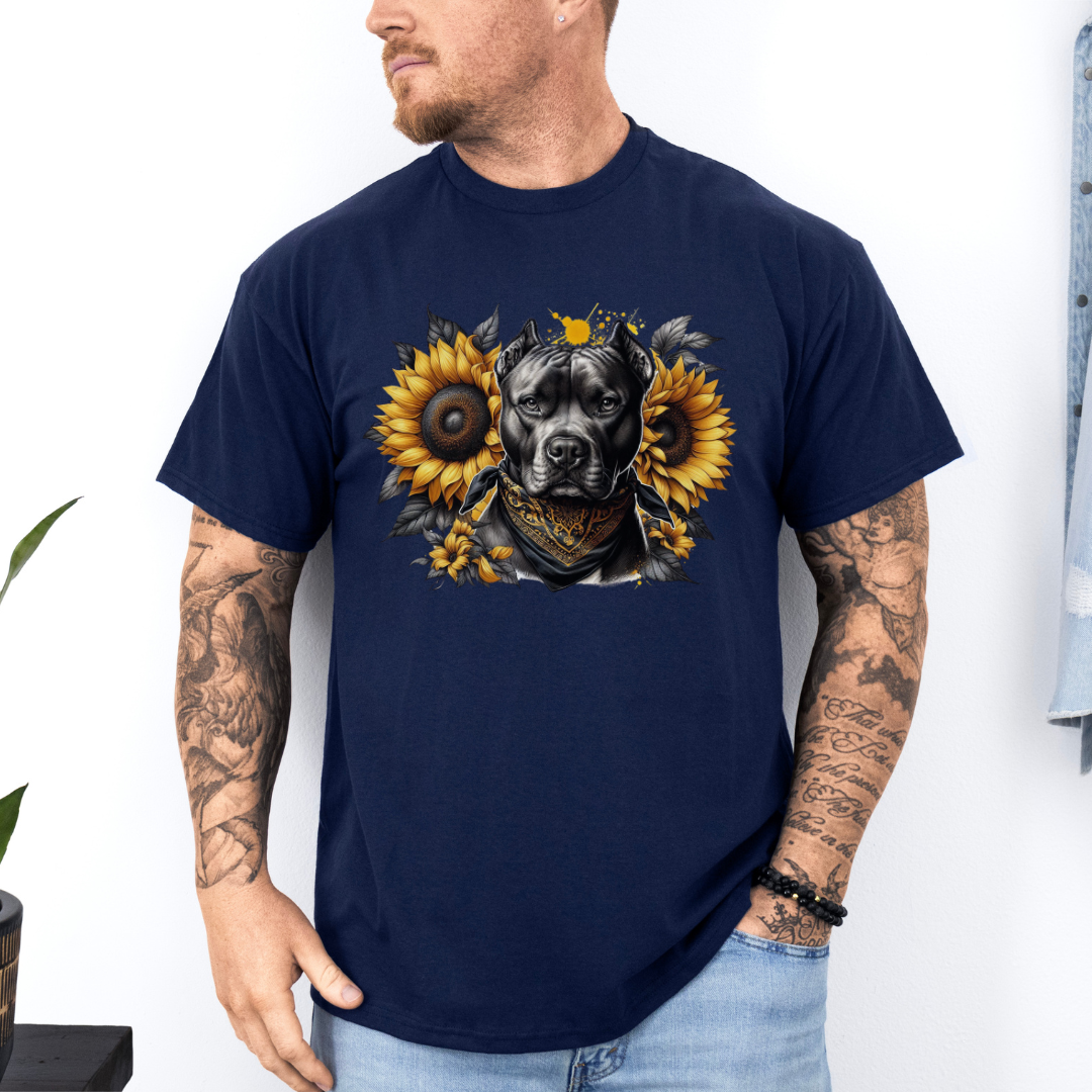 A man wearing a navy short-sleeve graphic t-shirt featuring a detailed print of a pitbull dog wearing a bandana and surrounded by yellow sunflowers. The man has tattoos on both arms and is wearing light blue jeans, standing against a white wall. Grab your tee from coffee and moo NZ.
