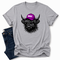 A heather gray short-sleeve t-shirt with a graphic of a black highland cow wearing a purple cap that says 'BOSSY' in white letters. The t-shirt is styled flat-lay with dark blue jeans on a white background. Grab your Bossy highland coo tee from Coffee and Moo NZ.