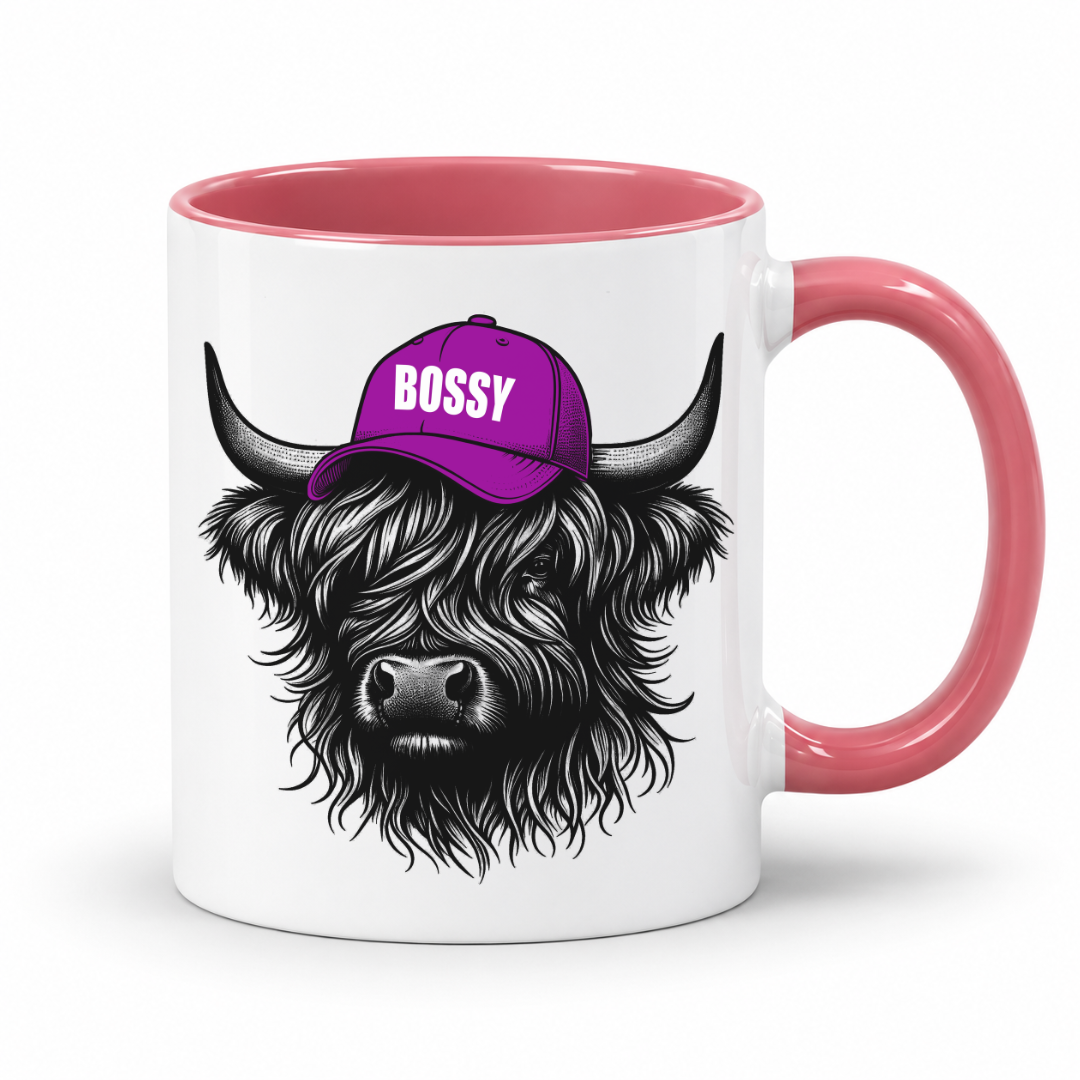 A white ceramic mug with a pink interior and handle, featuring a black-and-white illustration of a shaggy Highland cow wearing a purple cap with the word 'BOSSY' in white. Grab your bossy highland coo mug from Coffee and Moo NZ.