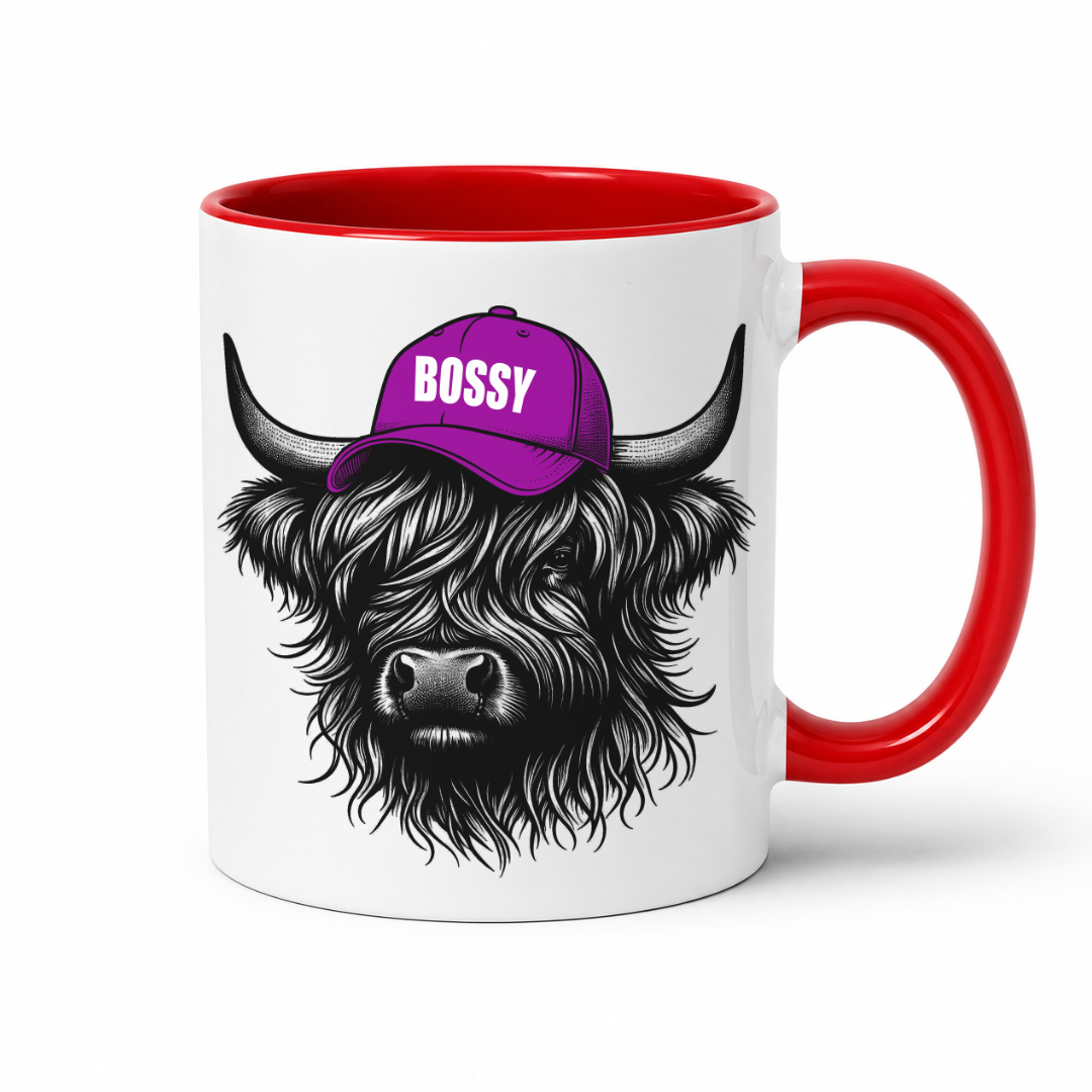 A white ceramic mug with a red handle and red interior, featuring a graphic of a shaggy Highland cow wearing a purple cap with the word 'BOSSY' in white text. Grab your bossy highland coo mug from Coffee and Moo NZ.