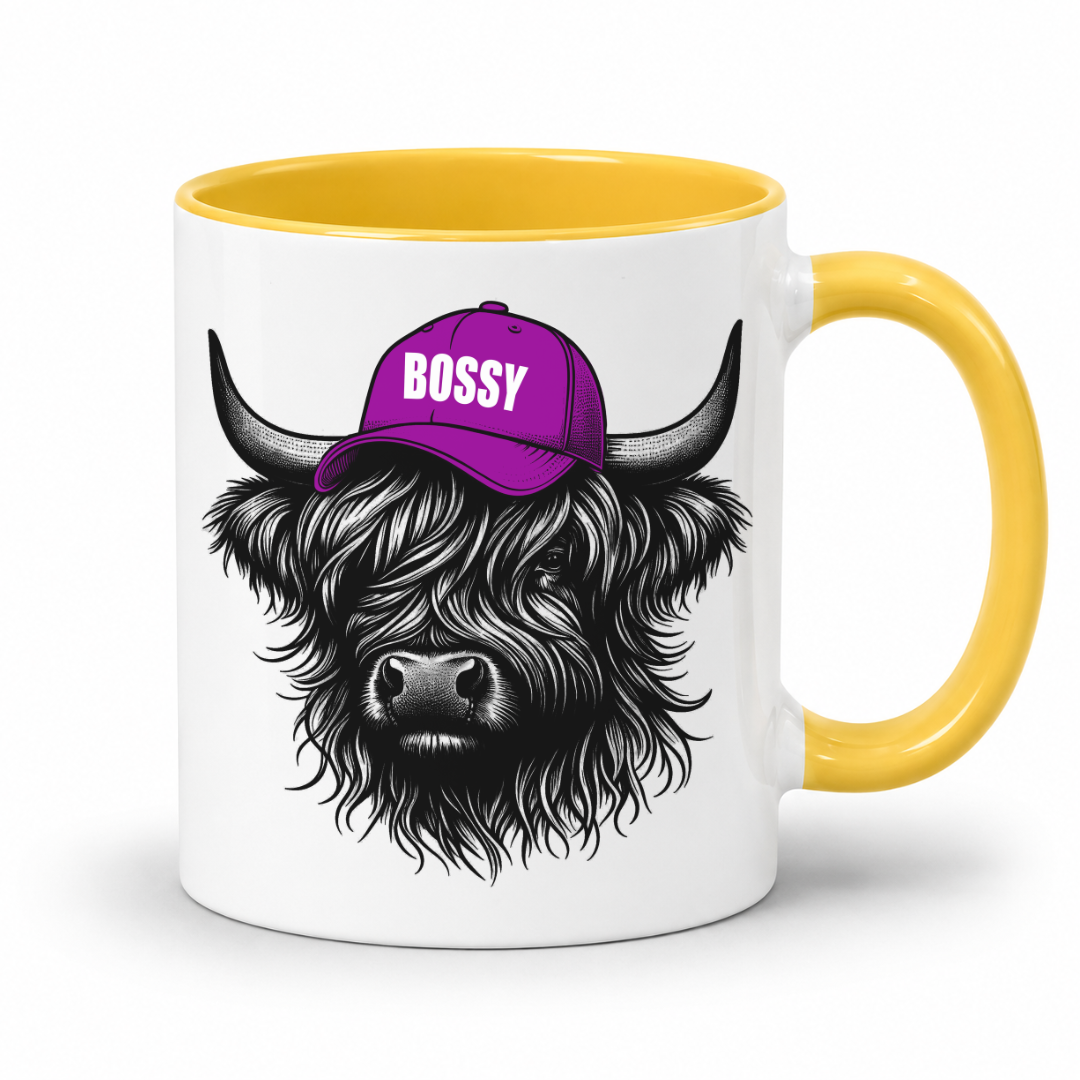 A white ceramic mug with a yellow interior and handle, featuring a black-and-white illustration of a shaggy Highland cow wearing a purple cap with the word 'BOSSY' in white. Grab your bossy highland coo mug from Coffee and Moo NZ.
