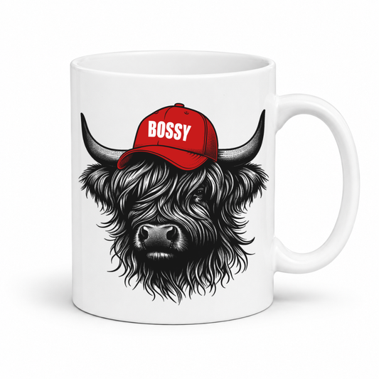A white ceramic mug featuring a graphic of a shaggy black-and-white Highland cow wearing a red baseball cap with the word 'BOSSY' in white, shown on a clean white background. Grab your Bossy highland coo mug from Coffee and Moo NZ.