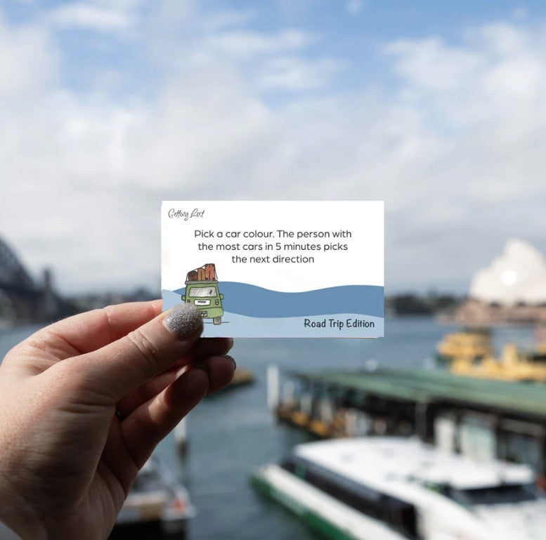 Image features a card from the Getting Lost Road Trip Edition Adventure Card Game with the text " Pick a car colour, the person with the most cars in 5 minutes picks the next direction". The pack features 26 direction + activity cards. Grab yours for your next road trip from Coffee and Moo NZ