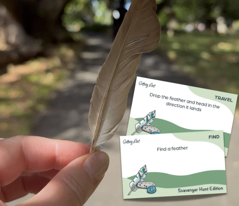 The Getting Lost Scavenger Hunt Edition. image shows 2 cards from the game. The cards show prompts like The cards read 'Getting Lost' and show simple illustrations with text such as 'Drop the feather and head in the direction it lands' and 'Find a feather. grab your game from coffee and moo NZ.