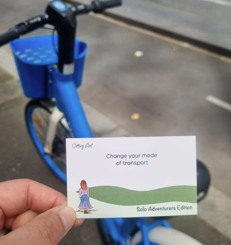 The Getting Lost Solo Adventurers Edition is your ultimate permit to escape the noise, skip the group compromises, and explore the world entirely at your own pace. the image shows a card that reads "change your mode of transport" Grab your game from Coffee and Moo NZ