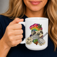 A woman holding a white ceramic mug featuring a colorful illustration of a sloth with red eyes, wearing a rainbow tie-dye beanie and holding a bong and baggy. Grab your mug from Coffee & Moo NZ