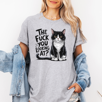 A woman wearing a grey graphic t-shirt with a black and white cat illustration and the text 'THE FUCK YOU LOOKING AT?'. She has a light blue denim jacket draped off her shoulders against a plain white background. Grab your feral tee from Coffee and Moo NZ.