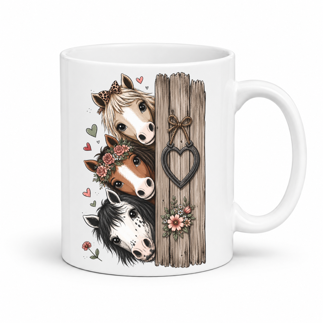 A white ceramic mug featuring a printed illustration of three horses peeking from behind a rustic wooden post with a heart-shaped ornament. From Coffee and Moo