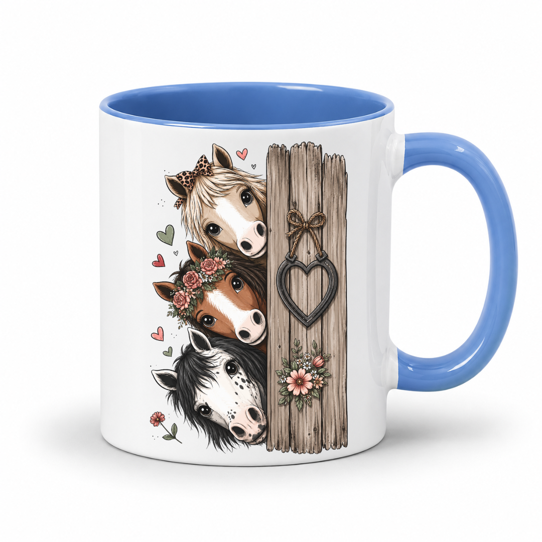 A white ceramic mug with a blue interior and handle, decorated with an illustration of three horse heads next to a rustic wooden post with a heart-shaped bow and flowers. From Coffee and Moo