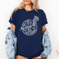 A woman wearing a navy graphic t-shirt with a white skeleton and text design Saying "when it comes to my child, i will smile in my mugshot" styled with an open light blue denim jacket and denim shorts. Purchase from Coffee and Moo NZ.