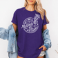 A woman wearing a purple graphic t-shirt with a white skeleton and text design Saying "when it comes to my child, i will smile in my mugshot" styled with an open light blue denim jacket and denim shorts. Purchase from Coffee and Moo NZ.