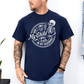 A man wearing a navy graphic t-shirt with a white skeleton and text design Saying "when it comes to my child, i will smile in my mugshot" styled with blue denim jeans. Purchase from Coffee and Moo NZ.
