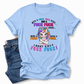 A light blue graphic t-shirt with a cartoon unicorn and profane text, styled flat-lay next to a pair of blue jeans on a white background.