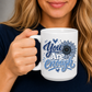 A woman holding a white ceramic mug with a blue graphic that reads 'You Are Enough' in stylized lettering with a sunflower design. Purchase yours from Coffee and Moo.