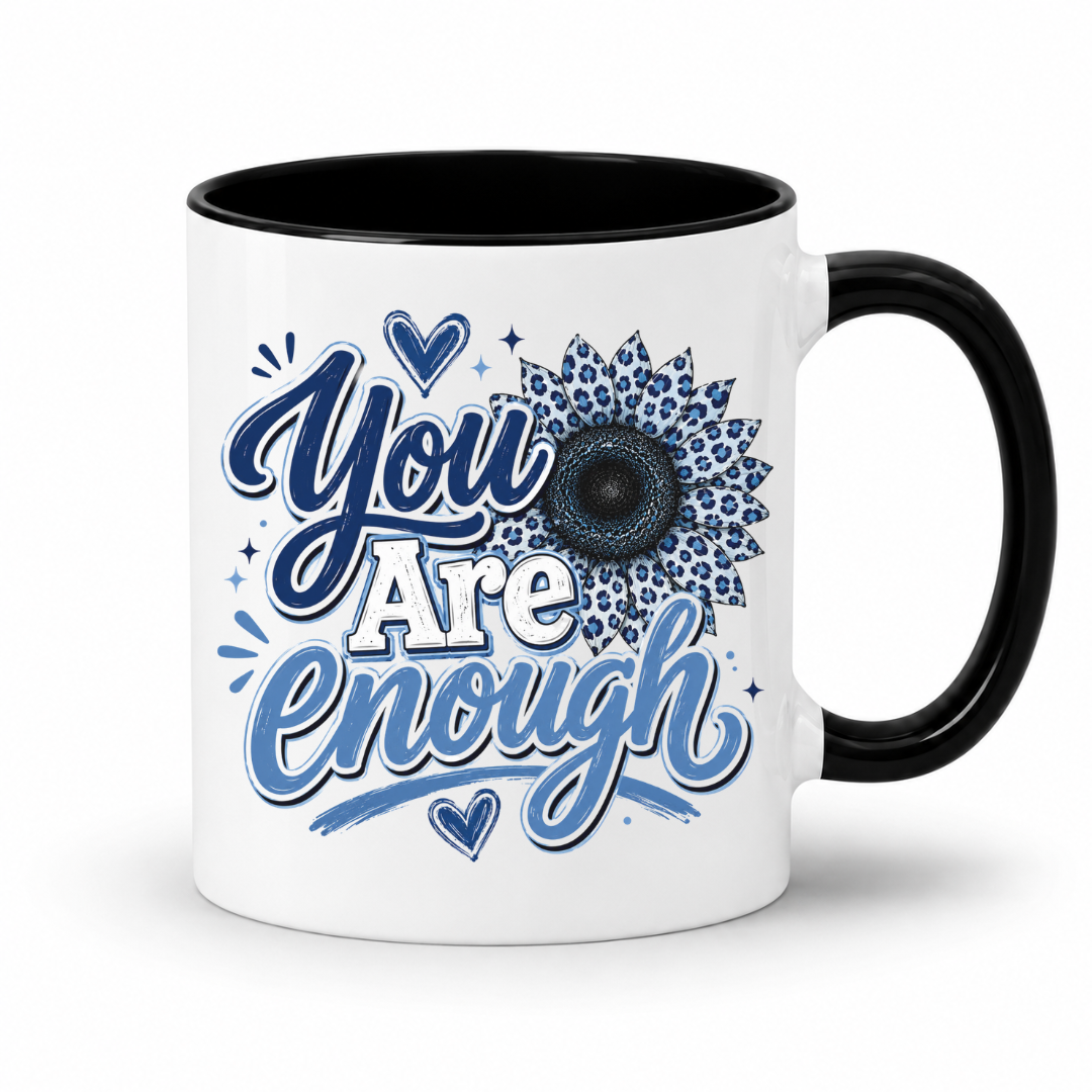 A white ceramic mug with a black interior and black handle, featuring a blue and white graphic design that reads 'You Are Enough' with a floral sunflower motif on the front. Purchase yours from Coffee and Moo.