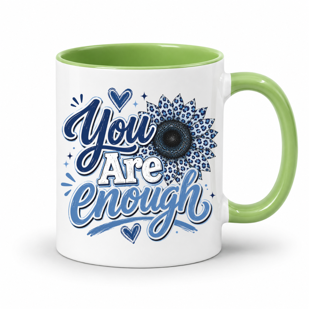 A white ceramic mug with a light green handle and interior, featuring a blue and white graphic that reads 'You Are Enough' with a floral sunflower design. Purchase yours from Coffee and Moo.