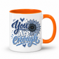 A white ceramic coffee mug with a bright orange handle and interior, featuring a blue graphic design on the front that reads 'You Are Enough' with a sunflower motif. Purchase yours from Coffee and Moo.