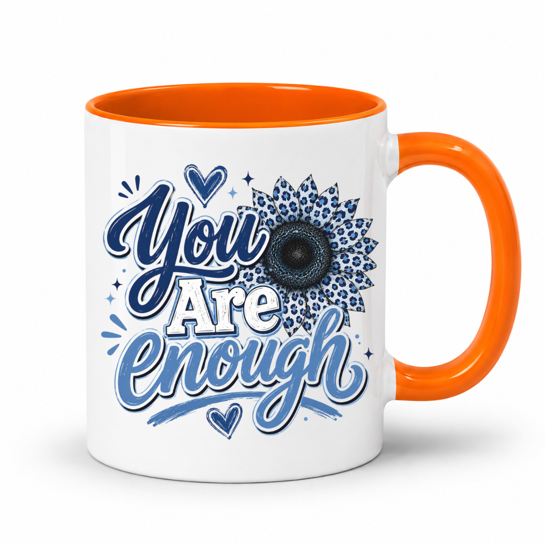 A white ceramic coffee mug with a bright orange handle and interior, featuring a blue graphic design on the front that reads 'You Are Enough' with a sunflower motif. Purchase yours from Coffee and Moo.