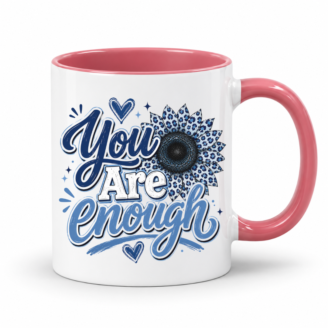 A white ceramic mug with a pink interior and handle, featuring the printed text 'You Are Enough' in blue and white script alongside a blue leopard-print sunflower design. Purchase yours from Coffee and Moo.
