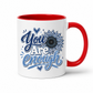 A white ceramic mug with a red interior and red handle, featuring the printed phrase 'You Are Enough' in blue and white script with a blue floral sunflower design on the front. Purchase yours from Coffee and Moo.