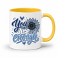 A white ceramic mug with a yellow interior and yellow handle, featuring the printed text 'You Are Enough' in blue and white script with a blue sunflower design on the front. Purchase yours from Coffee and Moo.