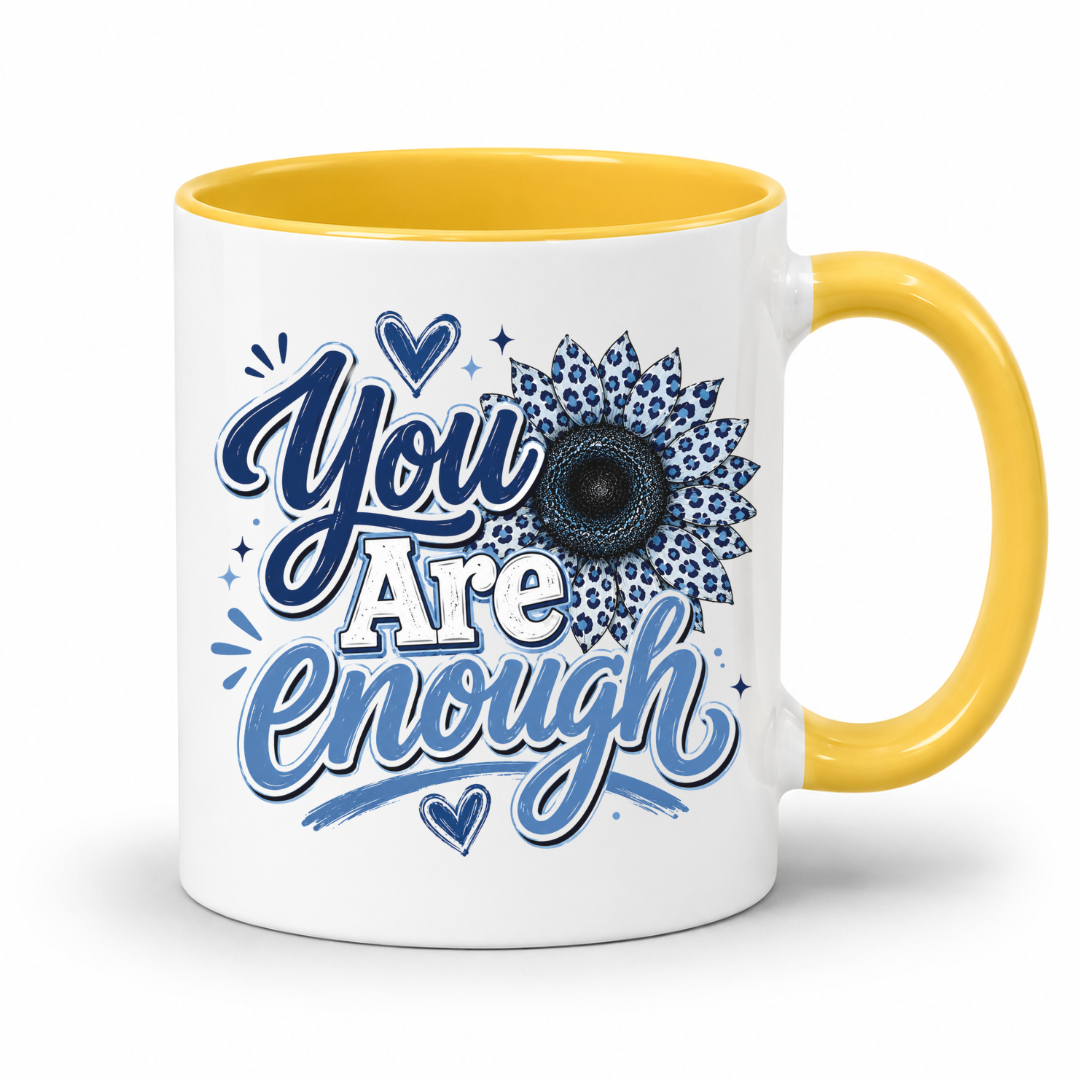 A white ceramic mug with a yellow interior and yellow handle, featuring the printed text 'You Are Enough' in blue and white script with a blue sunflower design on the front. Purchase yours from Coffee and Moo.