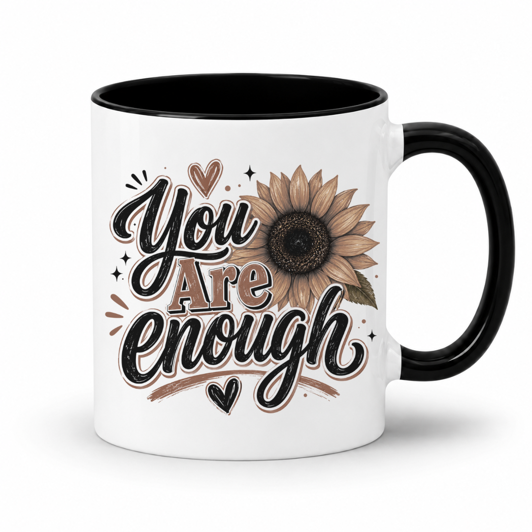 A white ceramic coffee mug, a black inner and handle, featuring a brown and black 'You Are Enough' typographic design featuring a brown sunflower, resting on a white background. Purchase yours from Coffee and Moo.