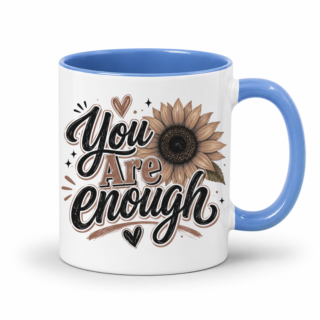 A white ceramic mug with a blue interior and handle, featuring a brown and black 'You Are Enough' typographic design featuring a brown sunflower, resting on a white background. Purchase yours from Coffee and Moo.