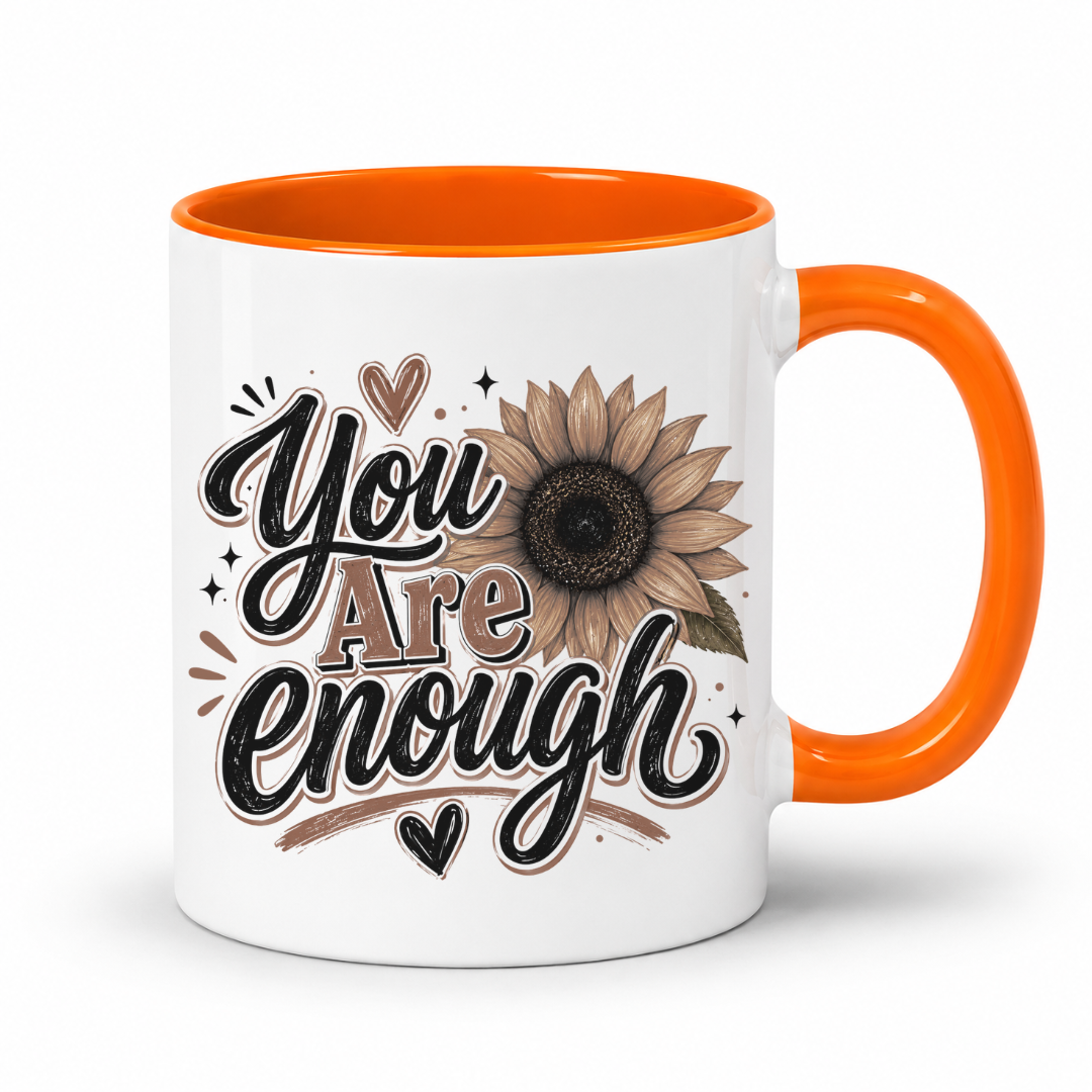 A white ceramic mug with a bright orange handle and interior, featuring a brown and black 'You Are Enough' typographic design featuring a brown sunflower, resting on a white background. Purchase yours from Coffee and Moo.