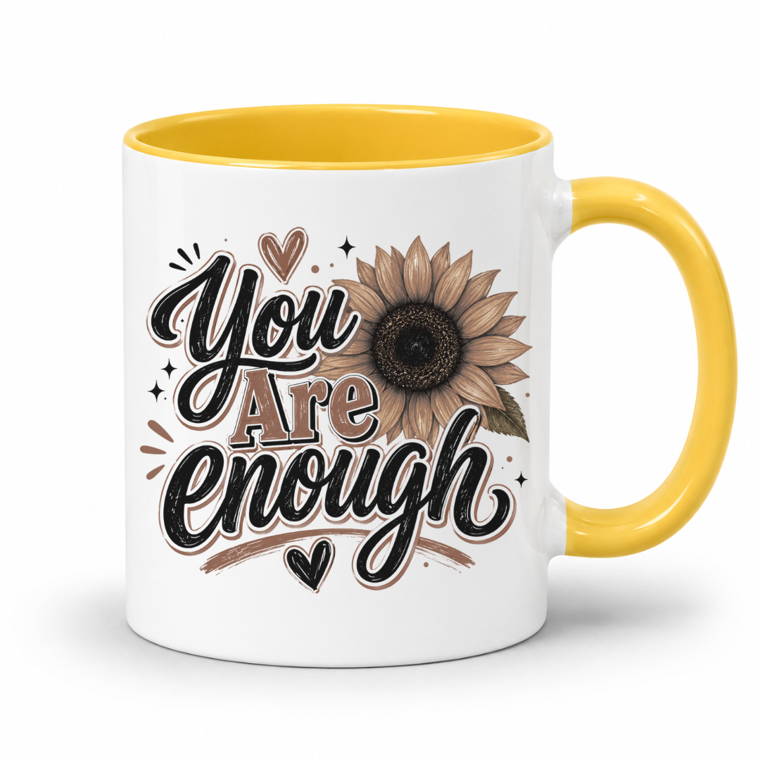 A white ceramic mug with a yellow interior and handle, featuring a brown and black 'You Are Enough' typographic design featuring a brown sunflower, resting on a white background. Purchase yours from Coffee and Moo.